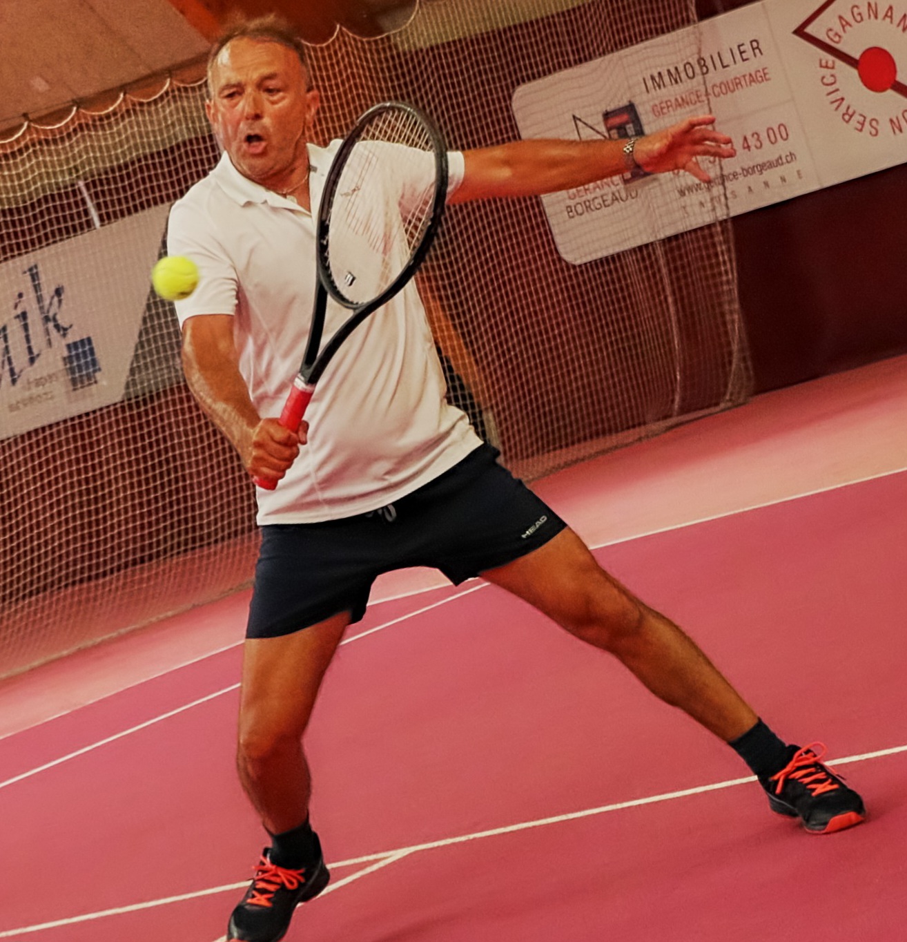 Pascual Alcaraz, coach de tennis, en plein revers sur un court couvert